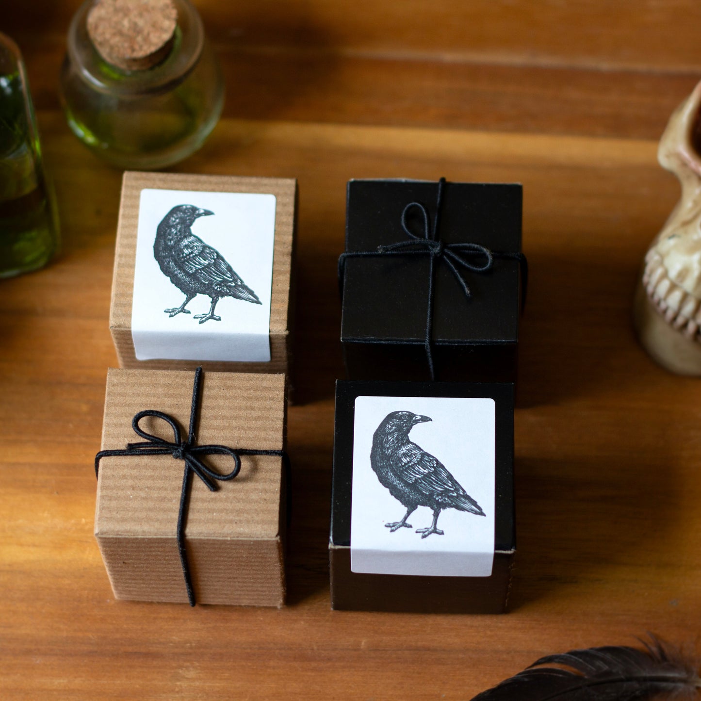Three small boxes with bird illustrations on a wooden surface, surrounded by bottles and a skull.