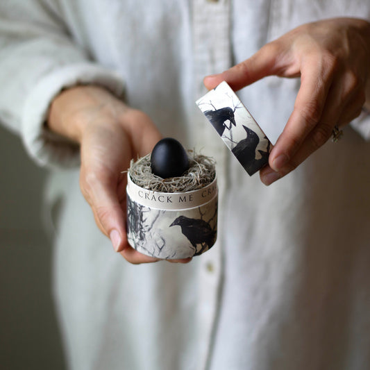 Person holding a small container with a black egg inside, labeled 'Crack Me'.