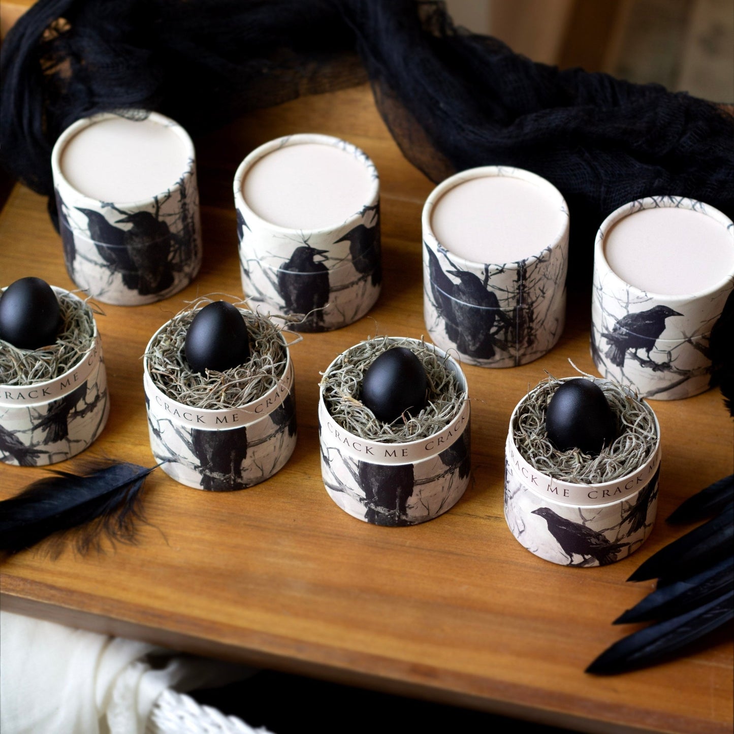 Decorative containers with Raven artwork on them black eggs on a wooden surface