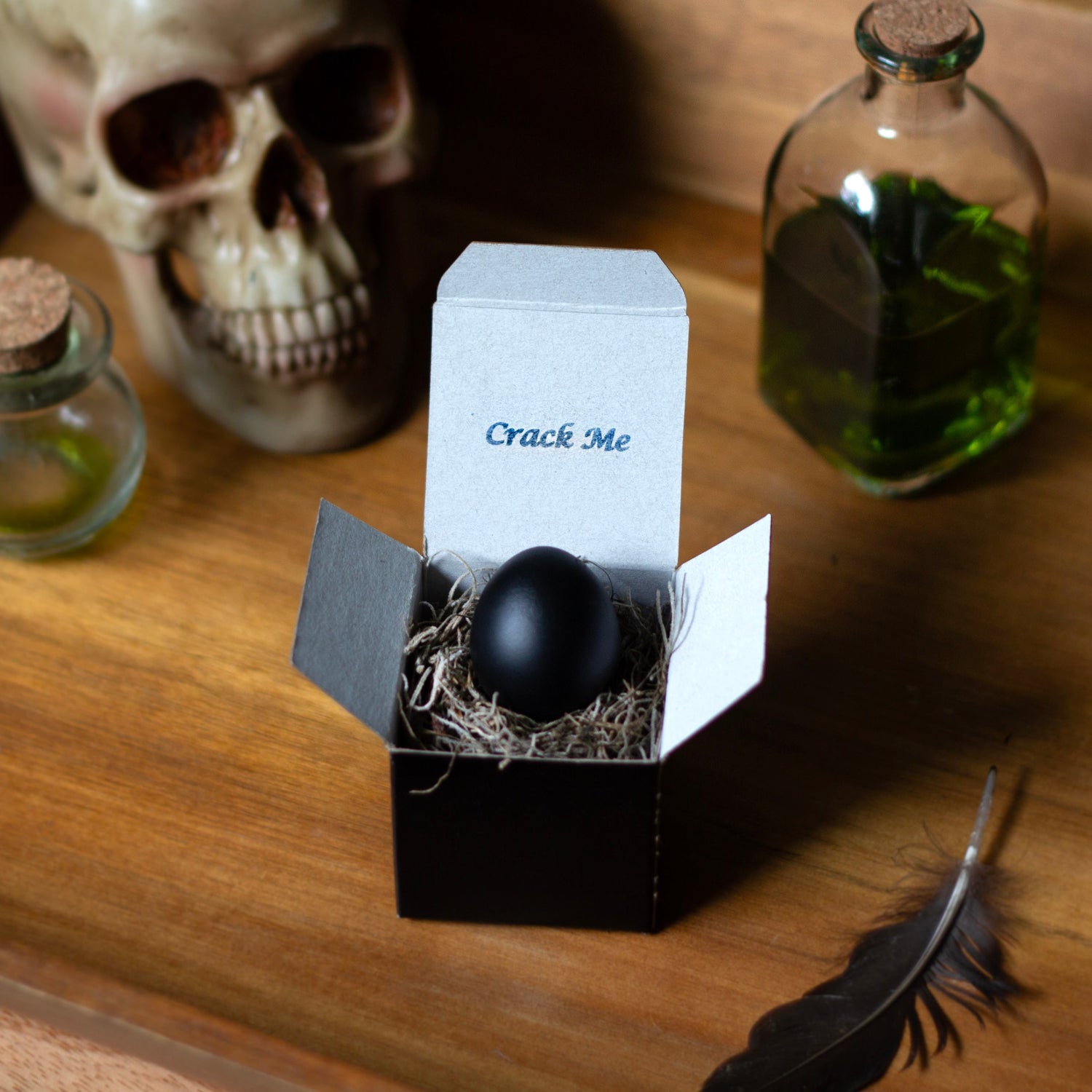 Black egg in a box labeled 'Crack Me' on a wooden surface with a skull and bottles in the background.