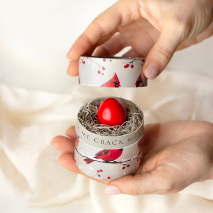 Hand holding a small container with a red egg and bird-themed design on a white background