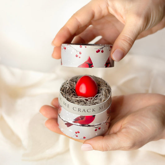 Hand holding a small container with a red egg and bird-themed design on a white background