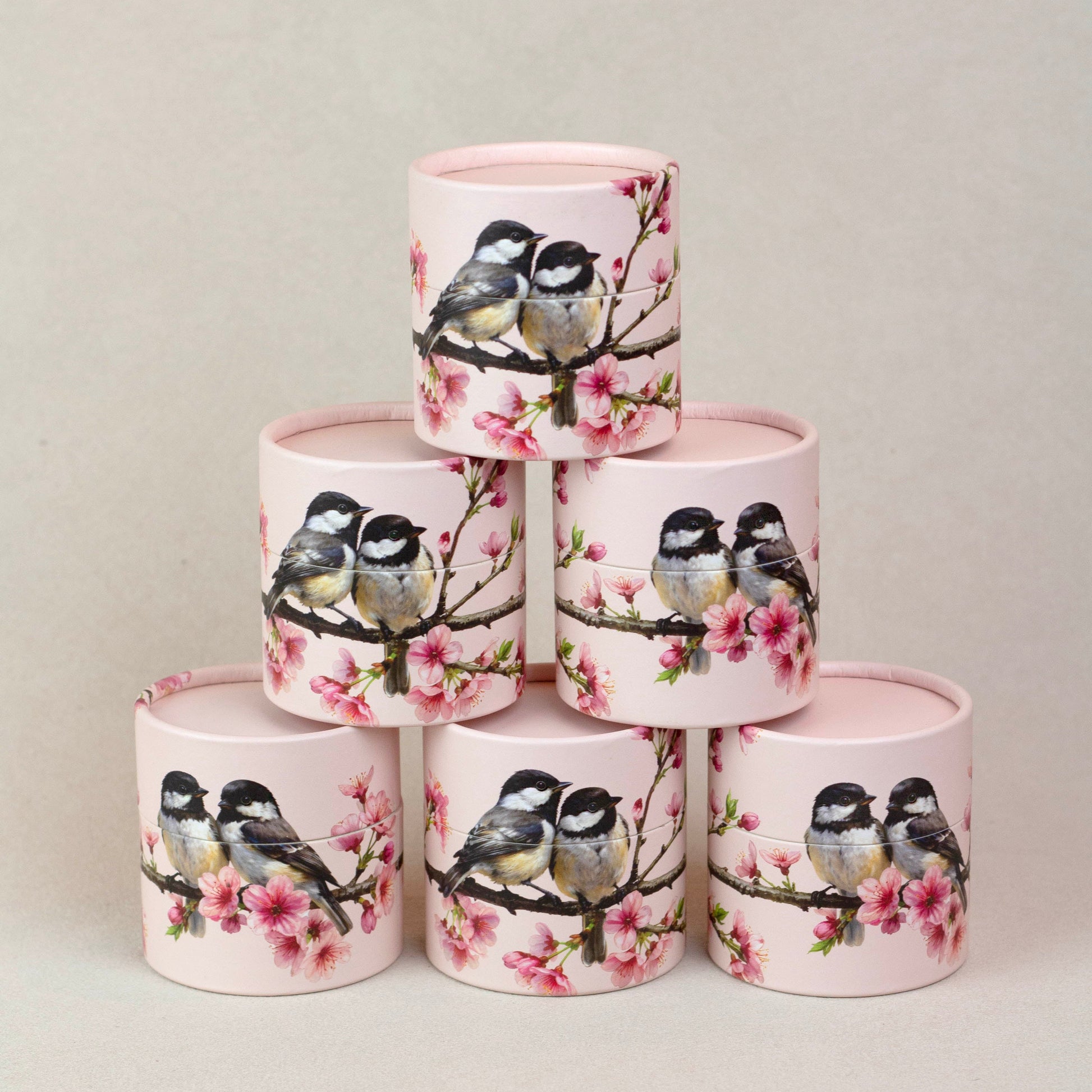 Stack of cylindrical containers with bird and floral design on a light gray background
