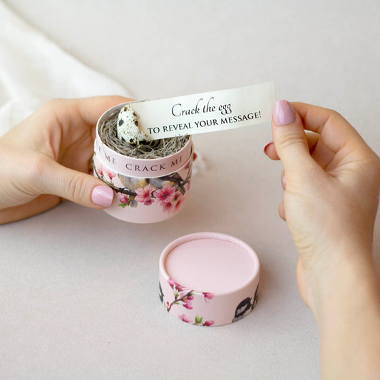 Person opening a small pink container with floral design to reveal a message strip.