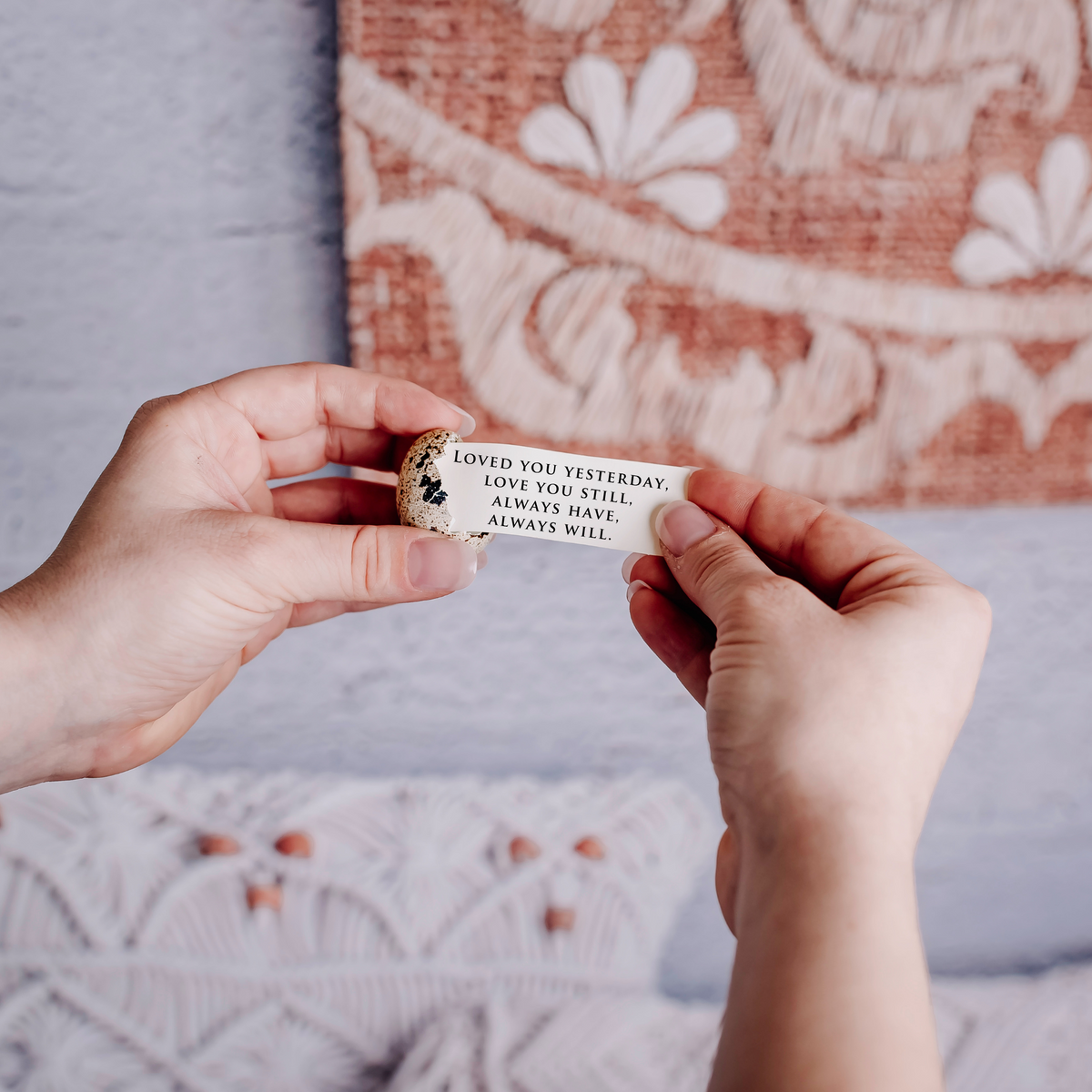 Hands hold a small quail egg that is cracked, and being pulled from the egg is a note that reads "loved you yesterday, love you still, always have, always will."