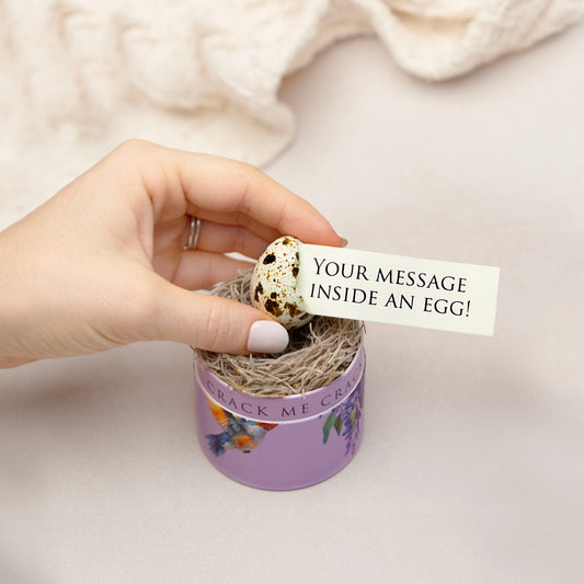 Hand holding a small quail egg inside a purple container with a tag reading 'Your message inside an egg!'.