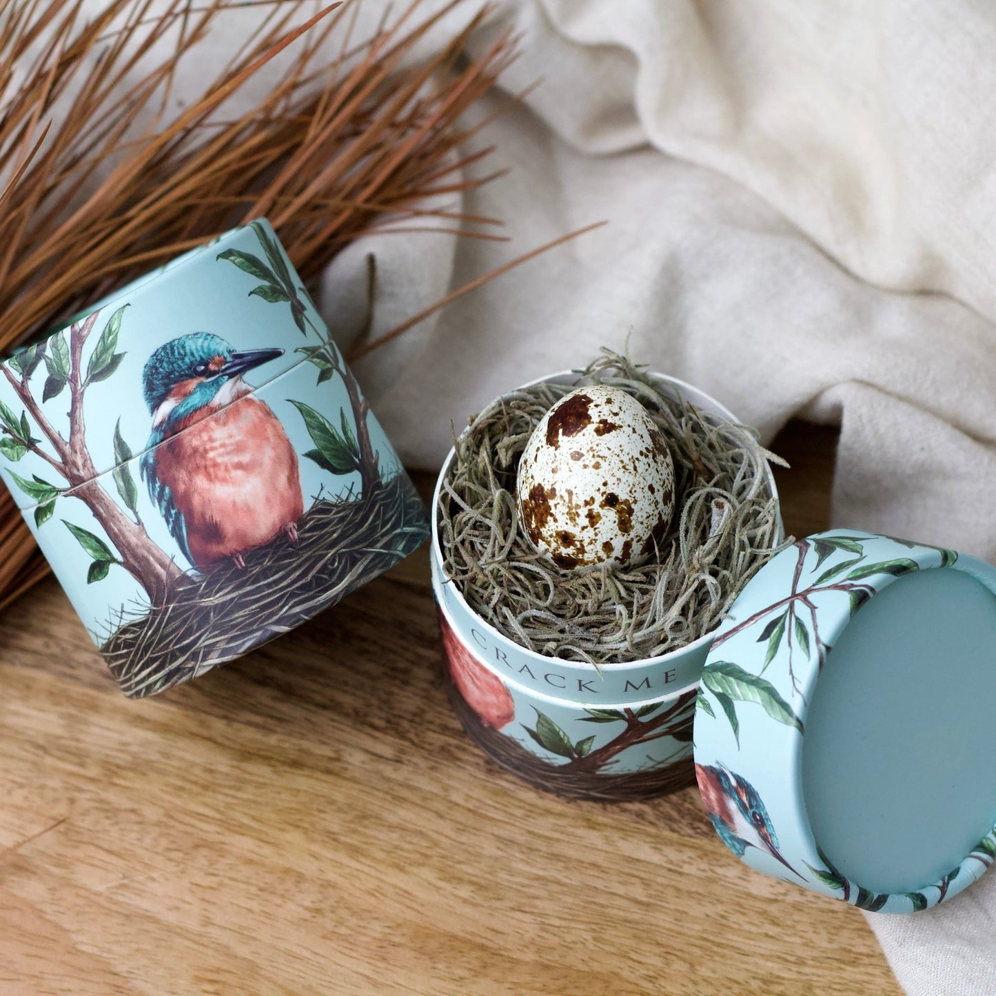 Decorative container with bird design and a small egg inside, on a wooden surface.