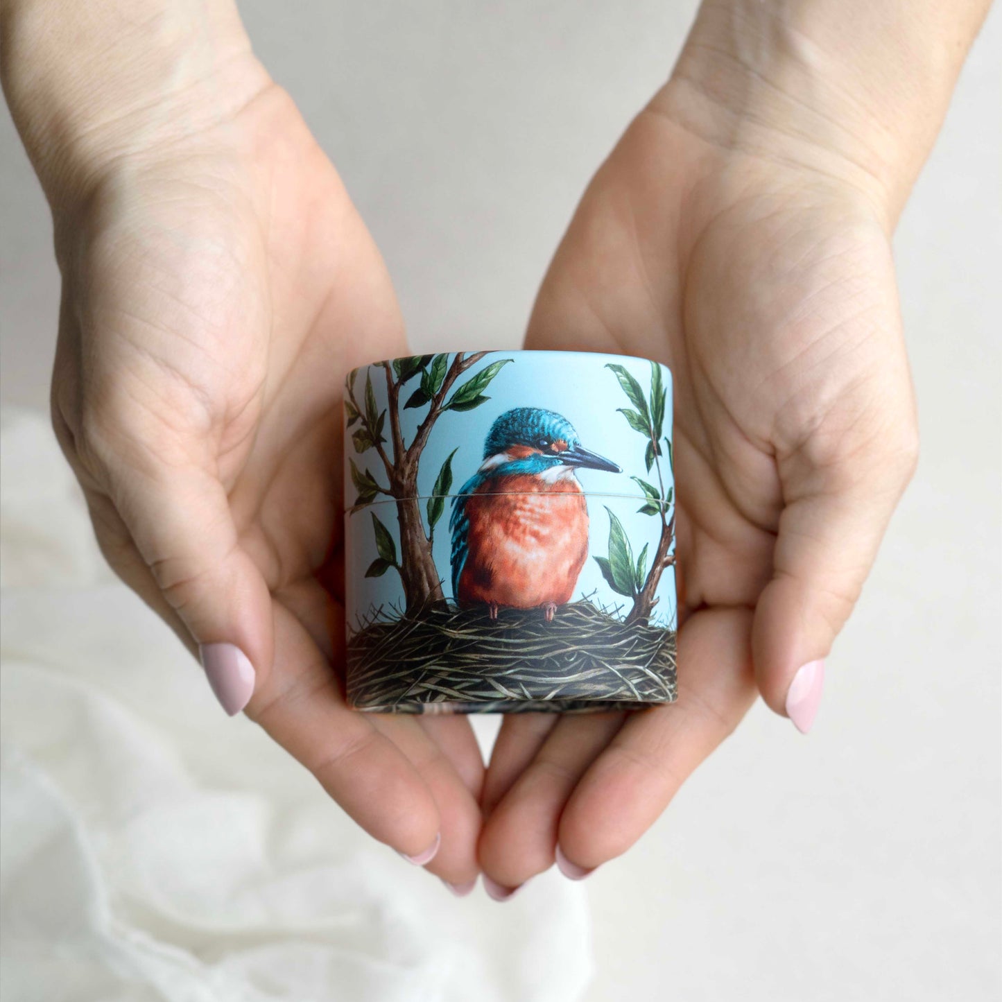 Hands holding a cylindrical container with a bird illustration on a light background