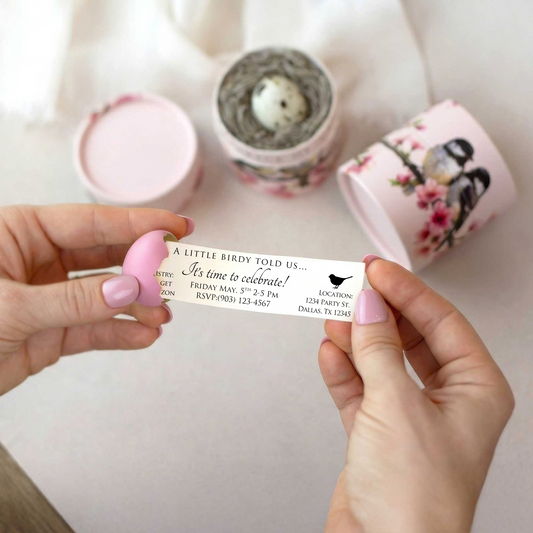 a pink egg is being held in someone's hands and is cracked. From within a small note scroll is being pulled out, with party invitation wording on it. 