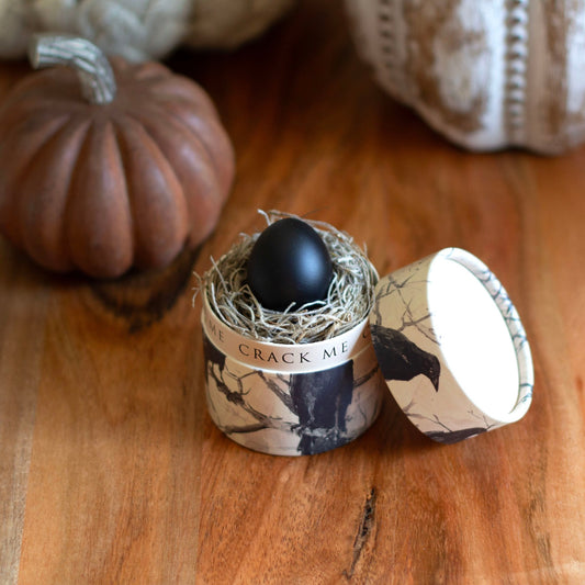 Small container with a black egg on a wooden surface with pumpkins in the background