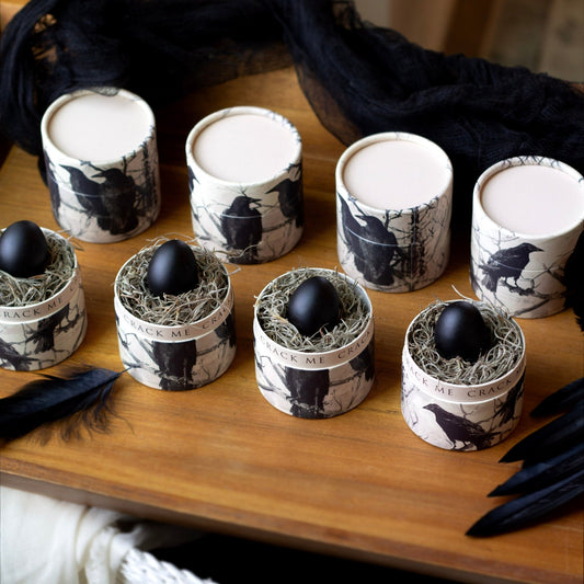 Decorative containers with Raven artwork on them black eggs on a wooden surface