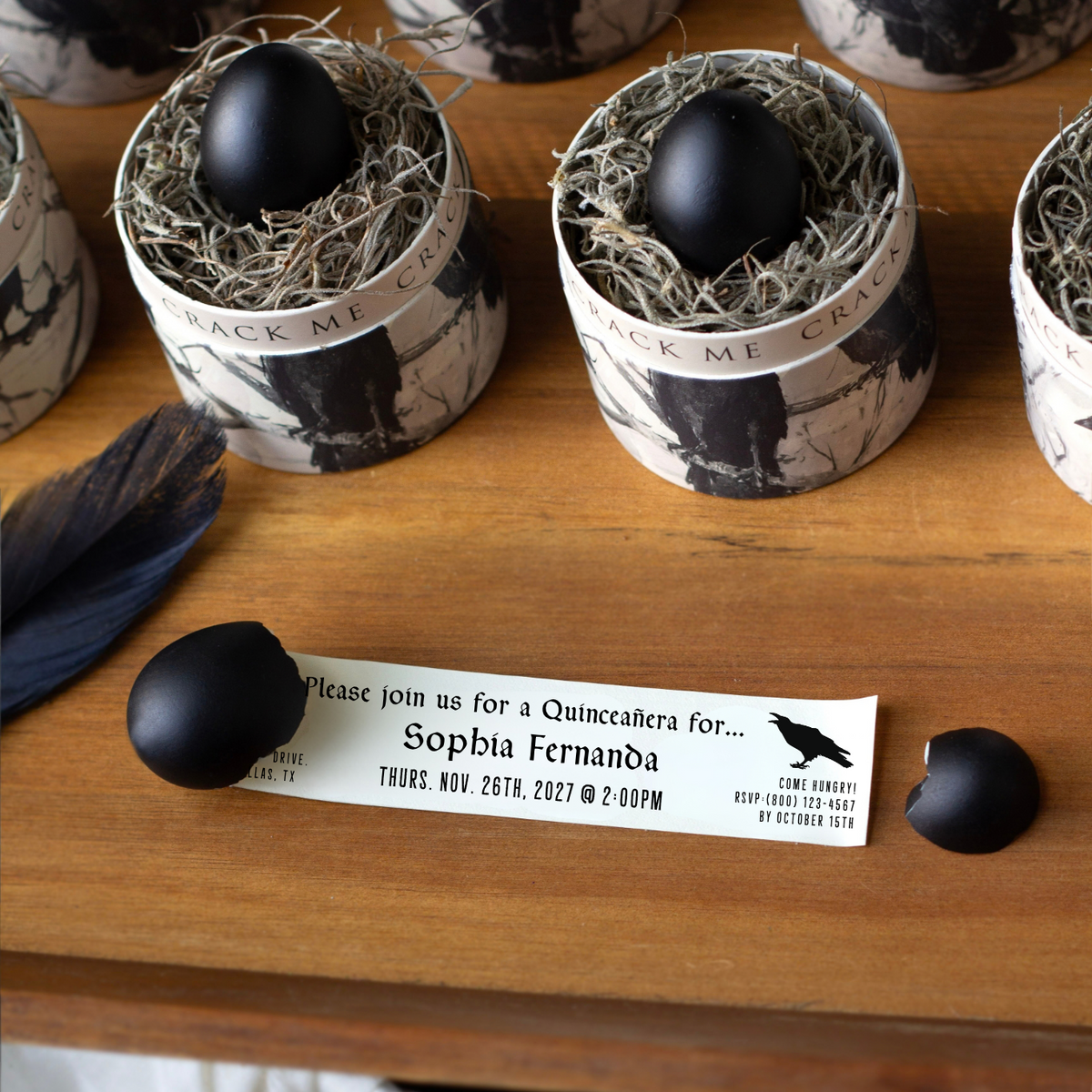 A small, black egg is cracked open, revealing what was inside of it - a quinceanera invitation on a small note scroll.  