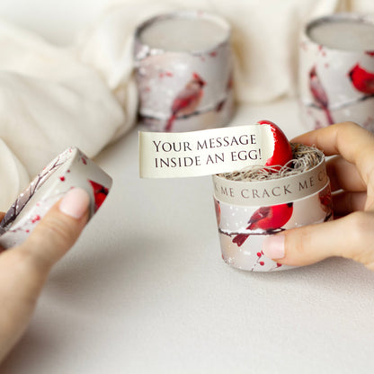 Small container with a red egg and a card inside, held by hands on a light background.